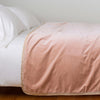 Harlow Blanket | Rouge | Cotton velvet bed end sized blanket, draped on a white bed - side view.