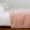 Harlow Blanket | Rouge | Cotton velvet blanket, draped on a white bed with corner folded back - side view.