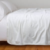 Harlow Blanket | White | Cotton velvet bed end sized  blanket, draped on a white bed - side view.