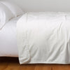 Harlow Blanket | Winter White | Cotton velvet bed end sized blanket, draped on a white bed with corner folded back - side view.