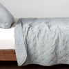 Harlow Coverlet | Cloud | Quilted cotton velvet coverlet, with top folded back to showcase linen back, draped over a white fitted sheet - side view.
