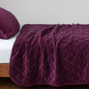 Harlow Coverlet | Fig | Quilted cotton velvet coverlet draped over a white fitted sheet - side view.
