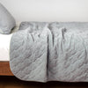 Harlow Coverlet | Mineral | Quilted cotton velvet coverlet draped over a white fitted sheet - side view.