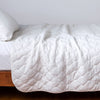 Harlow Twin Coverlet | White | Quilted cotton velvet coverlet draped over a white fitted sheet - side view.