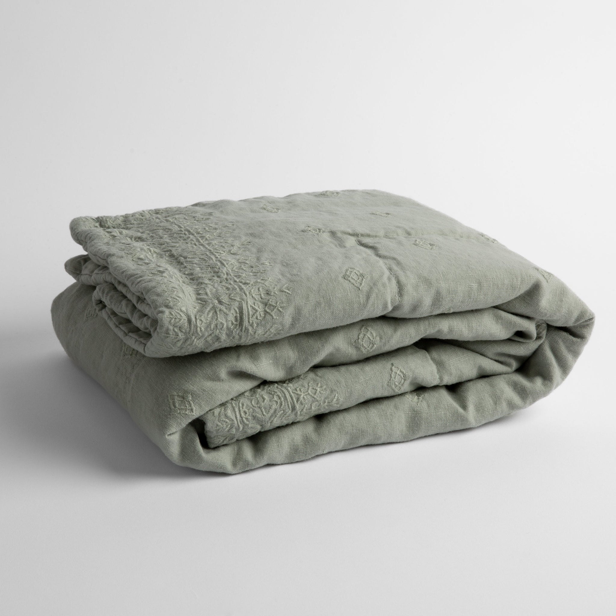 Ines Baby Blanket | Eucalyptus | embroidered linen baby blanket folded and shown  overhead from a slight angle against a white background.