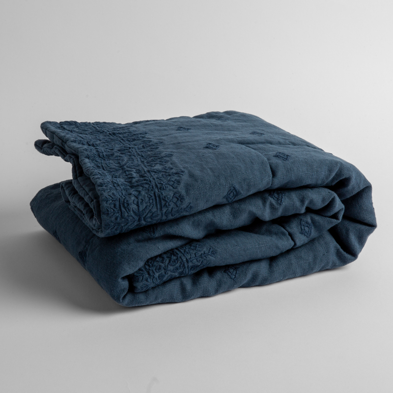 Ines Baby Blanket | Midnight | embroidered linen baby blanket folded and shown  overhead from a slight angle against a white background.