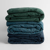 Ines Baby Blanket | a stack of three embroidered linen baby blankets in jade, cenote and midnight