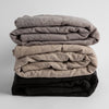 Ines Baby Blanket | A stack of three embroidered linen baby blankets in moonlight, fog and corvino. 