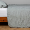 Ines Bedspread | Eucalyptus | embroidered midweight linen bedspread with matching sham on a bed with a white fitted sheet. Shot from the side view, the bedframe is slightly visible  against a white background and medium wood floor.