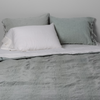 Ines Bedspread | Eucalpytus | Bedspread with matching shams on a bed with white sheets and sleeping pillows. Shot from the end of bed view, the flat sheet is pulled back over the top of the bedspread.