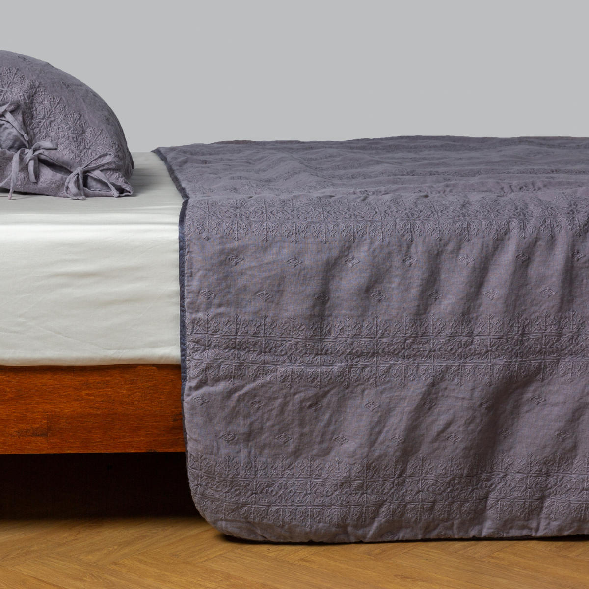Ines Bedspread | French Lavender | embroidered midweight linen bedspread with matching sham on a bed with a white fitted sheet. shot from the side view, the bedframe is slightly visible against a white background and medium wood floor.