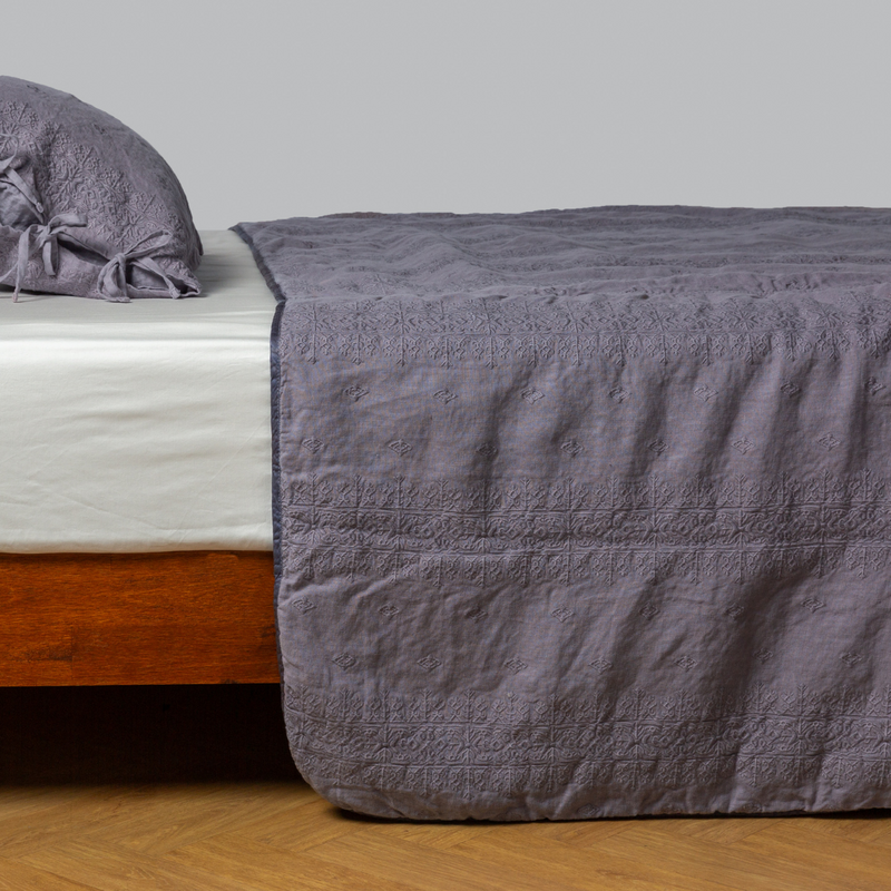 Ines Bedspread | French Lavender | embroidered midweight linen bedspread with matching sham on a bed with a white fitted sheet. shot from the side view, the bedframe is slightly visible against a white background and medium wood floor.