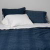 Ines Bedspread | Midnight | Bedspread with matching shams on a bed with white sheets and sleeping pillows. Shot from the end of bed view, the flat sheet is pulled back over the top of the bedspread.