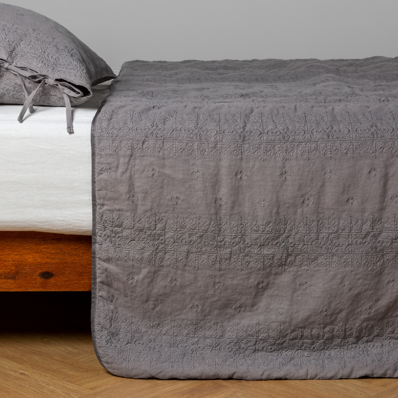 Ines Bedspread | Moonlight | embroidered midweight linen bedspread with matching sham on a bed with a white fitted sheet. Shot from the side view, the bedframe is slightly visible  against a white background and medium wood floor.