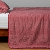 Ines Bedspread | Poppy | embroidered midweight linen bedspread with matching sham on a bed with a white fitted sheet. Shot from the side view, the bedframe is slightly visible  against a white background and medium wood floor.
