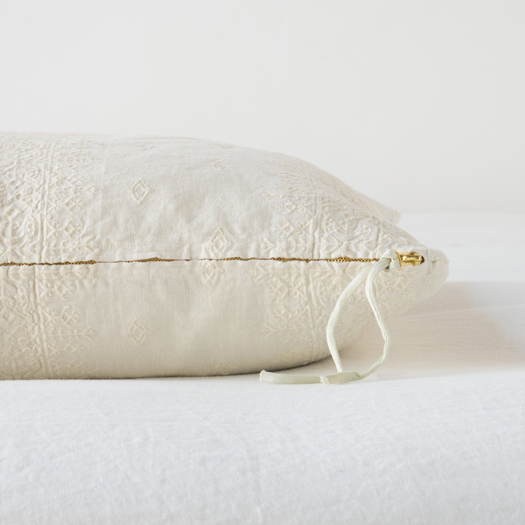 Ines Throw Pillow | Parchment | Close-up of brass zipper and charmeuse pull details on throw pillow - side view.