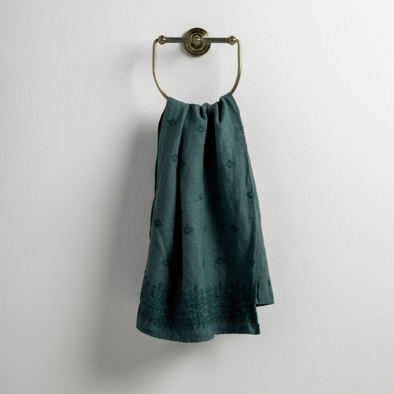 Ines Guest Towel | Cenote | guest towel draped through a decorative brass towel ring against a white background.