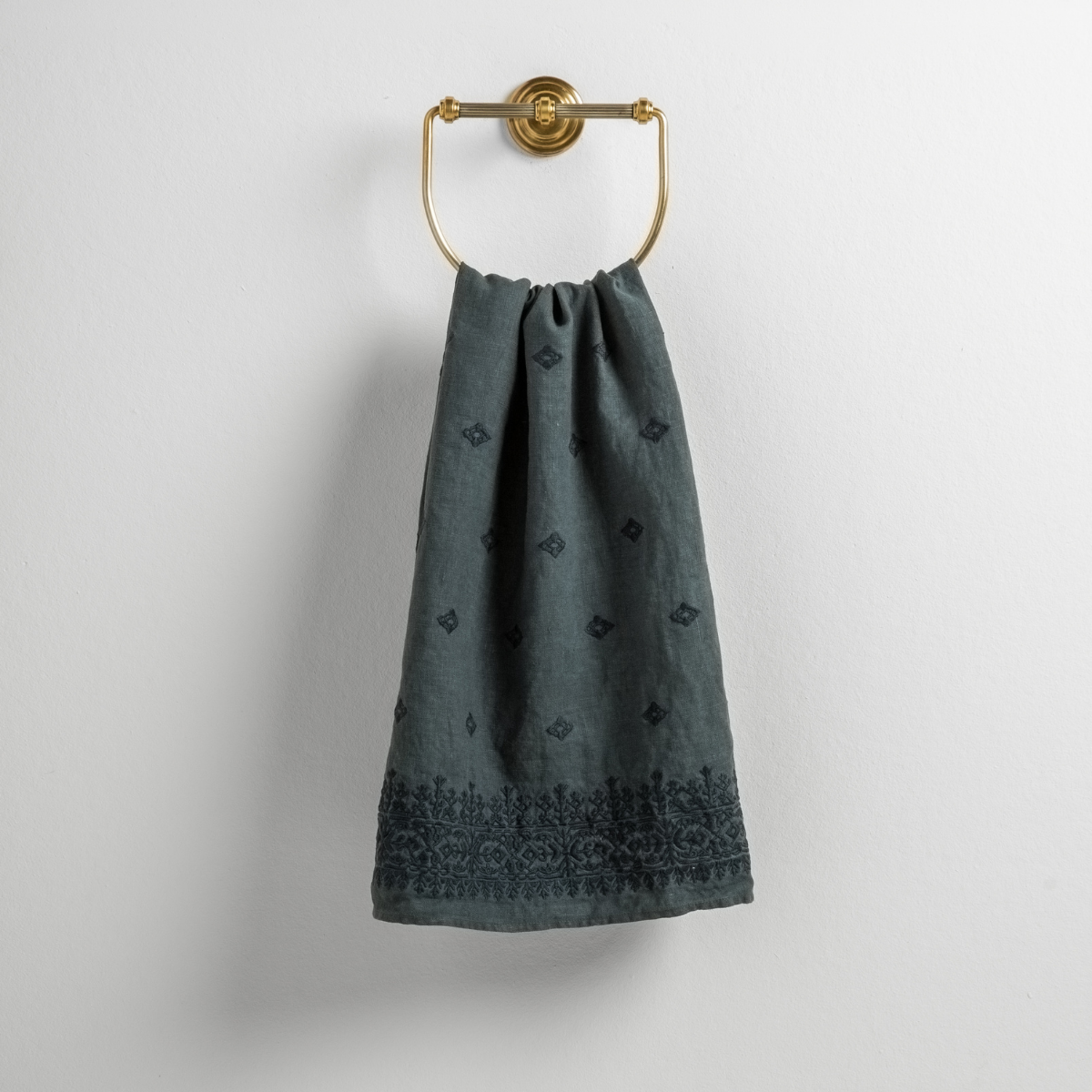Ines Guest Towel | Midnight | guest towel draped through a decorative brass towel ring against a white background.