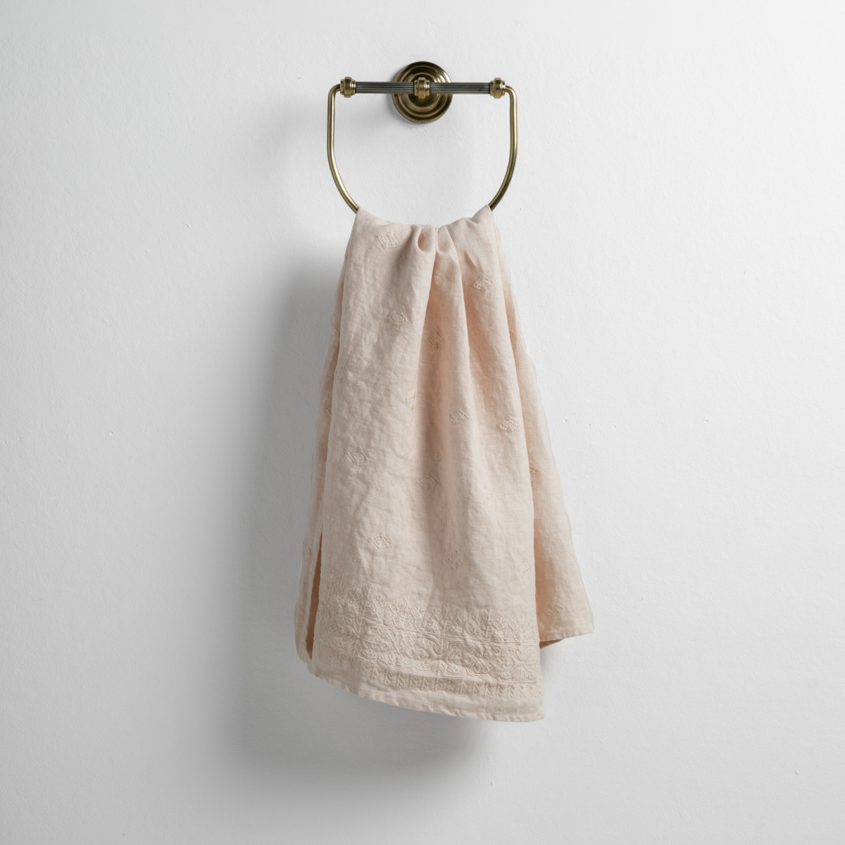 Ines Guest Towel | Pearl | guest towel draped through a decorative brass towel ring against a white background.