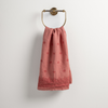 Ines Guest Towel | Poppy | guest towel draped through a decorative brass towel ring against a white background.