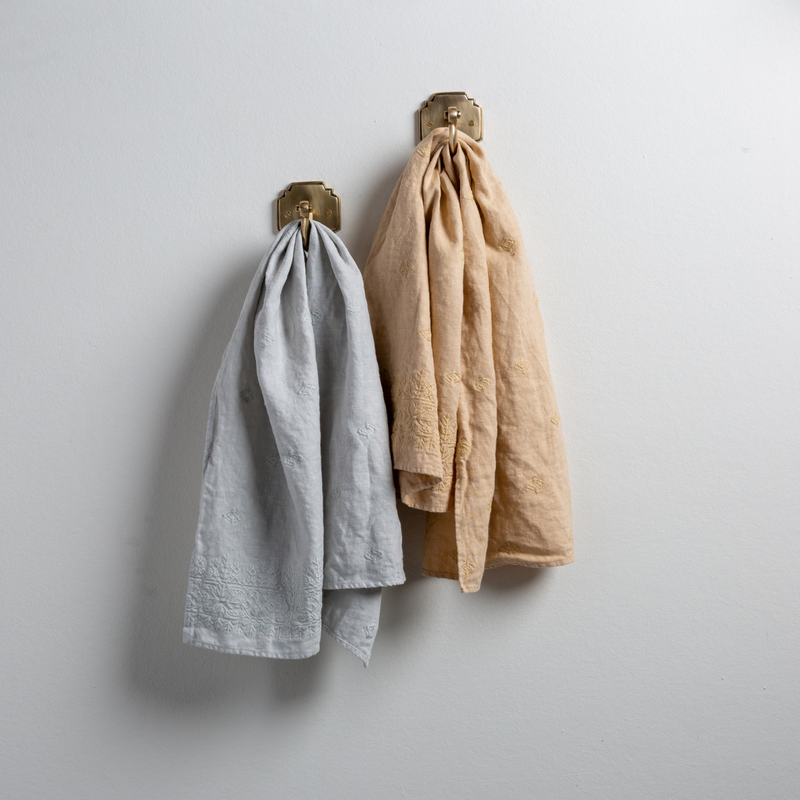Two Ines guest towels, draped over decorative hooks against a white wall - cloud and honeycomb.