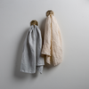 Two Ines guest towels, draped over decorative hooks against a white wall - cloud and parchment.