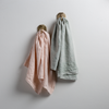 Two Ines guest towels, draped over decorative hooks against a white wall - pearl and eucalyptus.