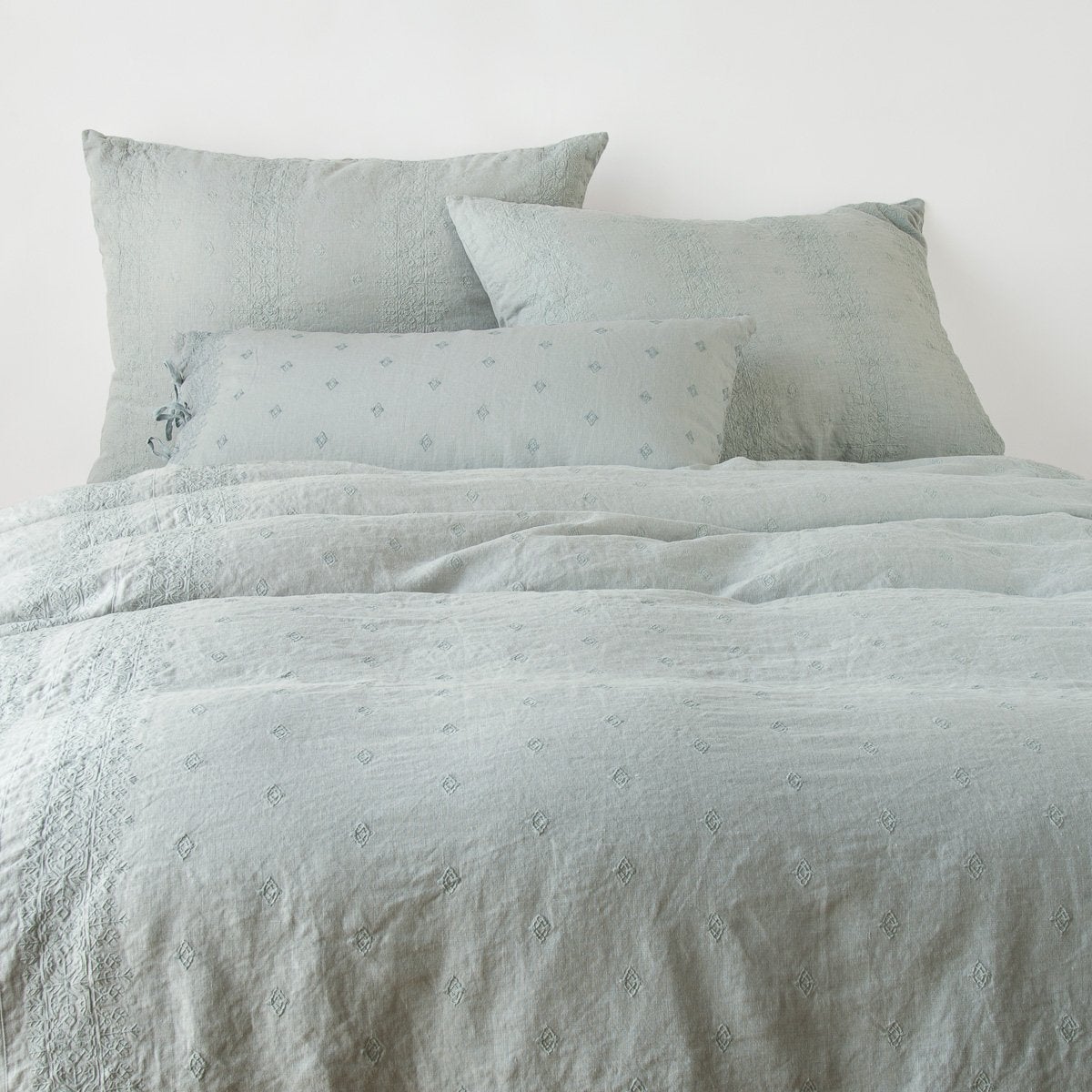 Ines Duvet Cover | Eucalyptus | duvet cover and matching shams against a white wall - end of bed view.