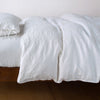 Ines Duvet Cover | White | lightly rumpled duvet cover on a monochromatic bed against a white background - side view.