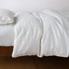 Ines duvet cover in winter white, lightly rumpled on a monochromatic bed against a plain background - side view.