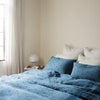 Midnight | Midnight Ines duvet cover and shams, layered with soft green linen pillows, with light toned walls and curtains, all bathed in natural light - cropped three-quarter angle.