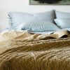 Ines Sham | Cloud | Ines standard shams in cloud, layered behind on-tone linen sheets and silk charmeuse sleeping pillows, and a rumpled silk velvet quilted coverlet in a rich golden tone - cropped head-on view.