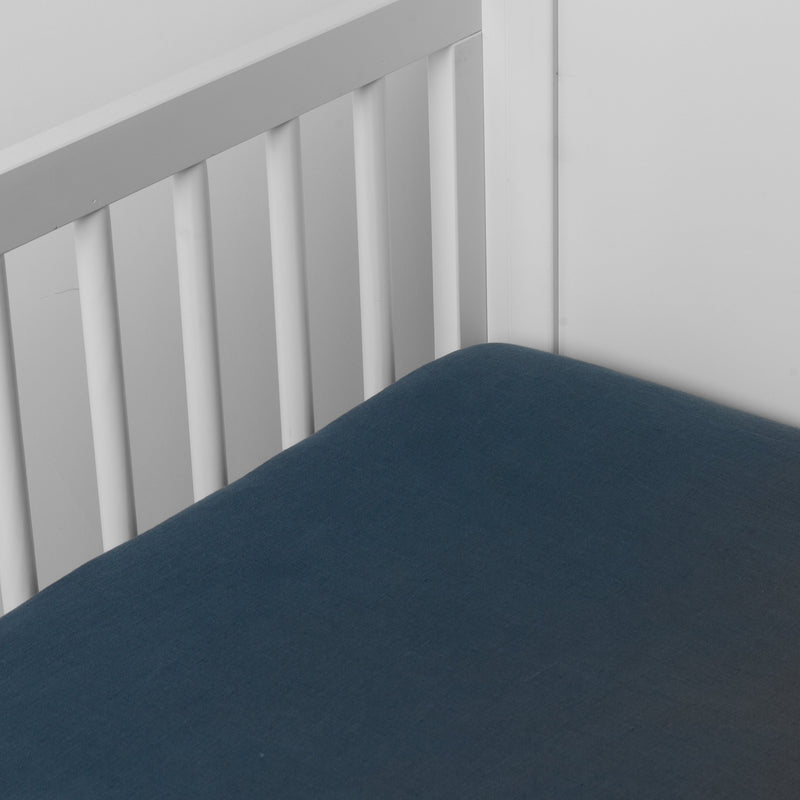 Midnight | linen crib sheet on the mattress shot slightly overhead into the corner of a white crib. against a white background.