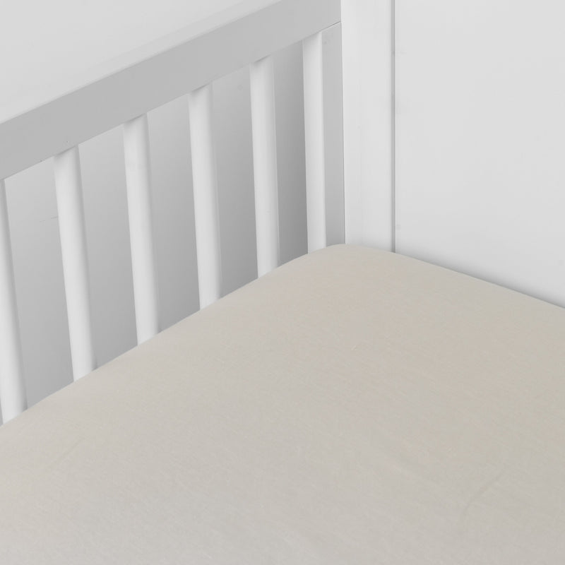 Parchment | linen crib sheet on the mattress shot slightly overhead into the corner of a white crib. against a white background.