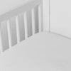 White | linen crib sheet on the mattress shot slightly overhead into the corner of a white crib. against a white background.