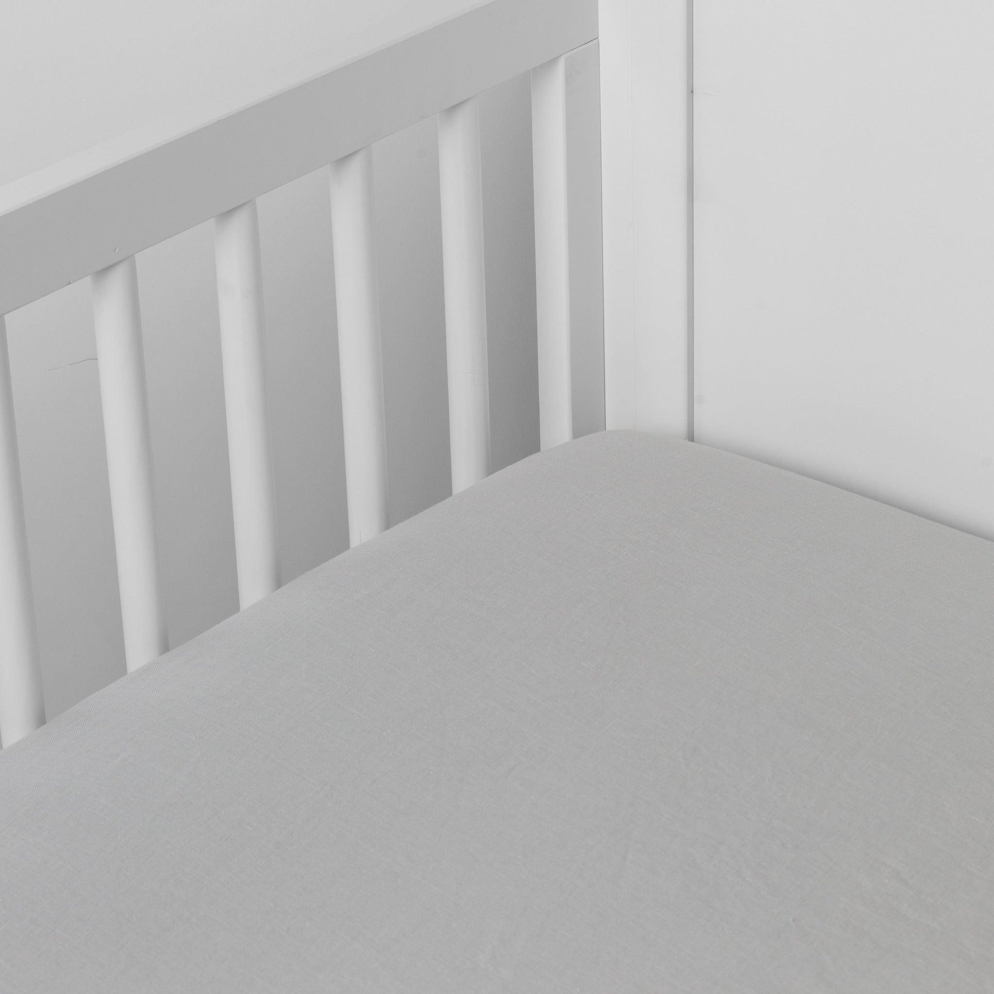Cloud | linen crib sheet on the mattress shot slightly overhead into the corner of a white crib. against a white background.