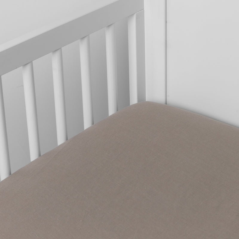 Fog | linen crib sheet on the mattress shot slightly overhead into the corner of a white crib. against a white background.