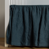 Linen Crib Skirt | Midnight | crib skirt shown on a white crib with no mattress against a white wall and medium wood flooring.