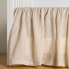 Linen Crib Skirt | Parchment | crib skirt shown on a white crib with no mattress against a white wall and medium wood flooring.