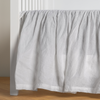 Linen Crib Skirt | White | crib skirt shown on a white crib with no mattress against a white wall and medium wood flooring.