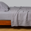 Linen Fitted Sheet | French Lavender | side view of a matching linen fitted, flat and pillowcase shown on a medium wood bed frame against a white background.