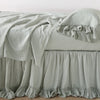 Linen Whisper Bed Skirt | Eucalyptus | bed skirt layered with monochromatic linen sheeting - side view.