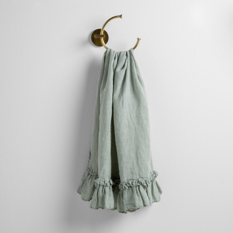 Linen Whisper Guest Towel | Eucalyptus | guest towel draped through a decorative brass towel ring, against a white wall.