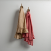 Two Linen Whisper guest towels, draped over decorative hooks against a white wall - honeycomb and poppy.
