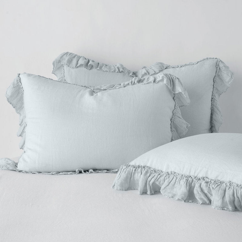Linen Whisper Sham | Cloud | two shams leaning upright and one laying flat at an angle in the foreground, against a blank background.