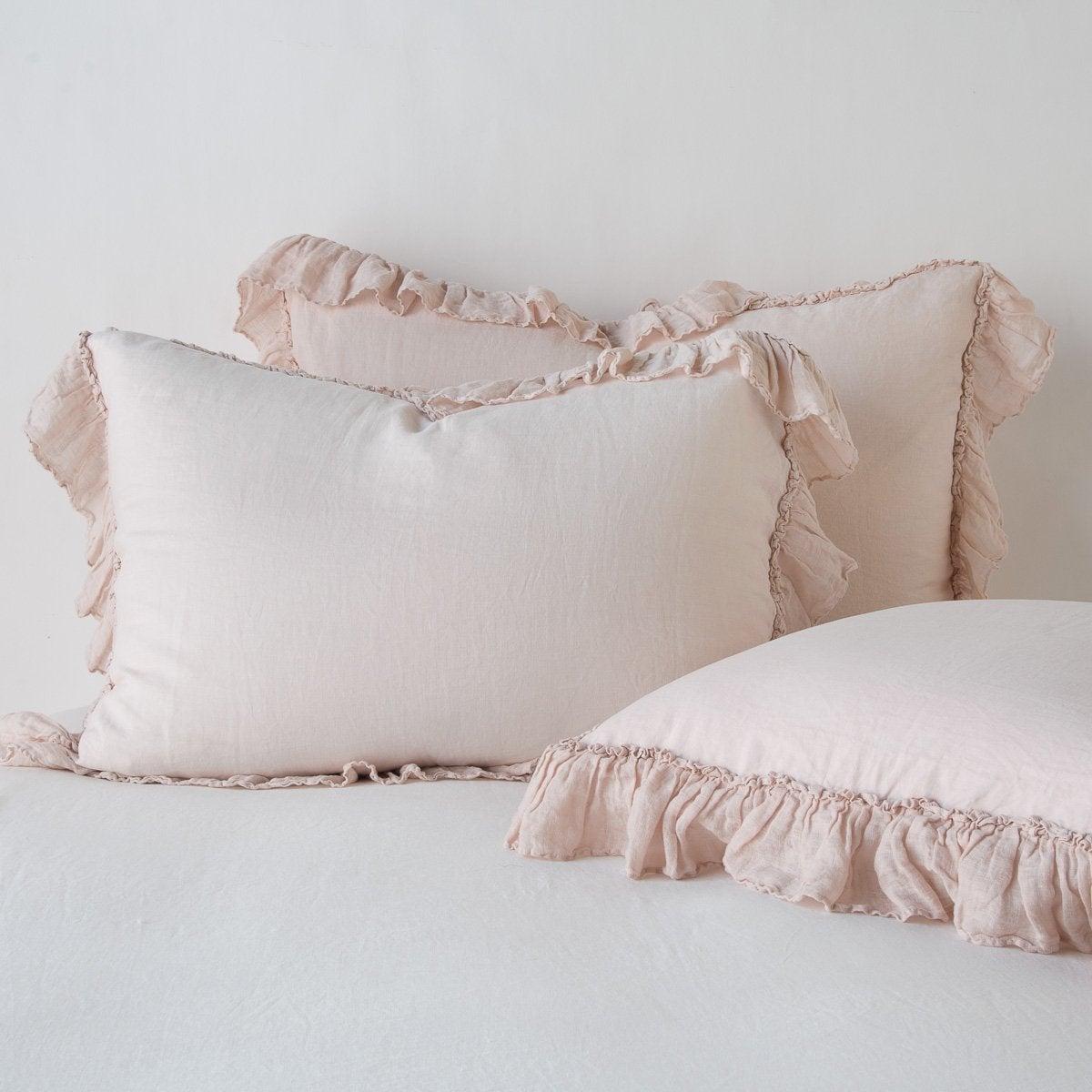 Linen Whisper Sham | Pearl | two shams leaning upright and one laying flat at an angle in the foreground, against a blank background.