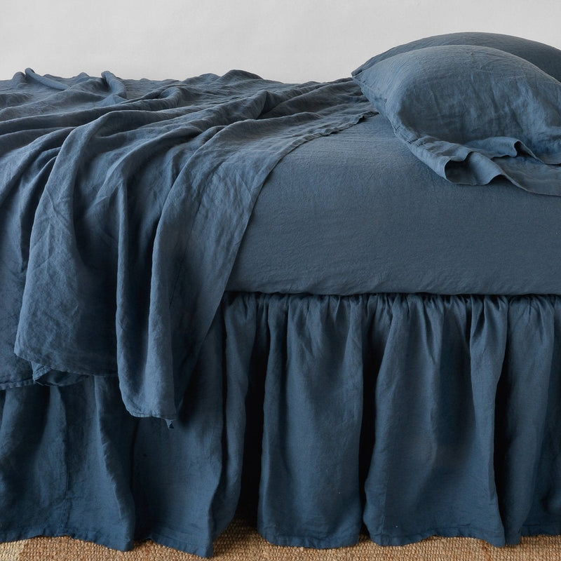 Linen Twin Bed Skirt | Linen bed skirt in midnight, with matching rumpled sheets and sleeping pillows - side view.