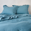 Linen Duvet Cover | Cenote | duvet cover partially folded back on a bed with matching sheets and shams against a white wall - cropped end of bed view.
