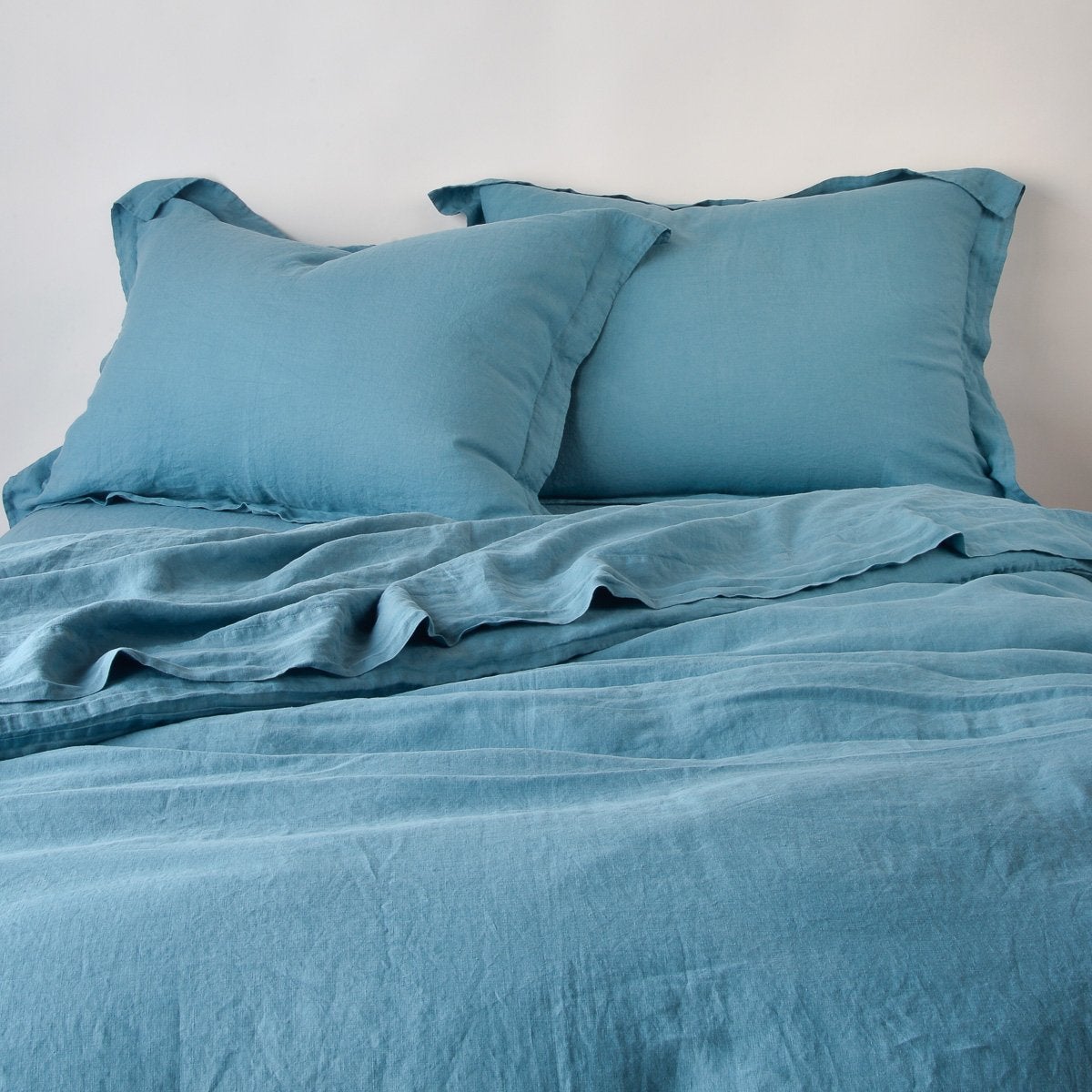 Linen Duvet Cover | Cenote | duvet cover partially folded back on a bed with matching sheets and shams against a white wall - cropped end of bed view.