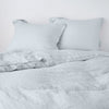 Linen Twin Duvet Cover | Cloud | duvet cover partially folded back on a bed with matching sheets and shams against a white wall - cropped end of bed view.